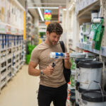 Cliente em um corredor de uma loja de impermeabilizantes segurando um rolo de pintura