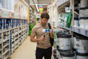 Cliente em um corredor de uma loja de impermeabilizantes segurando um rolo de pintura